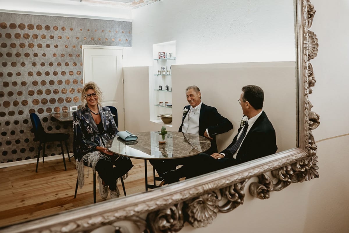 Matrimonio a "La Madernassa" nelle Langhe sotto la pioggia. preparazione dello sposo. Sposo sorseggia un caffè con il testimone ed un'amica. Riflessi in uno specchio.