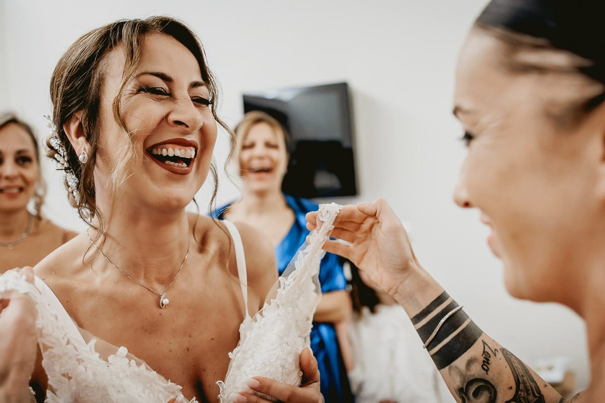 Matrimonio a "La Madernassa" nelle Langhe sotto la pioggia. Preparazione della sposa. Sposa ride con la damigella.