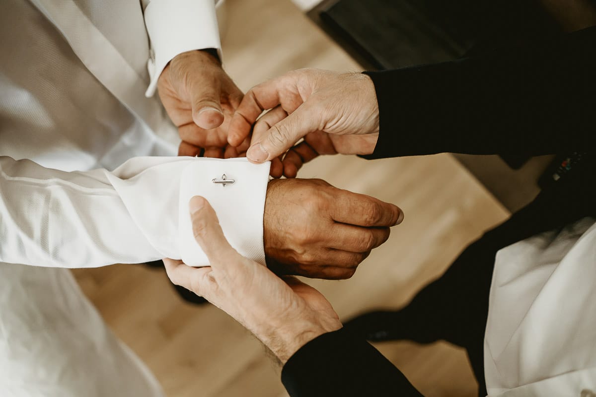 Matrimonio a "La Madernassa" nelle Langhe sotto la pioggia. preparazione dello sposo. Testimone sistema i gemelli ai polsini della camicia.
