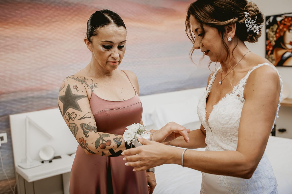 Matrimonio a "La Madernassa" nelle Langhe sotto la pioggia. Preparazione della sposa. Sposa mette il corsage ad una damigella.