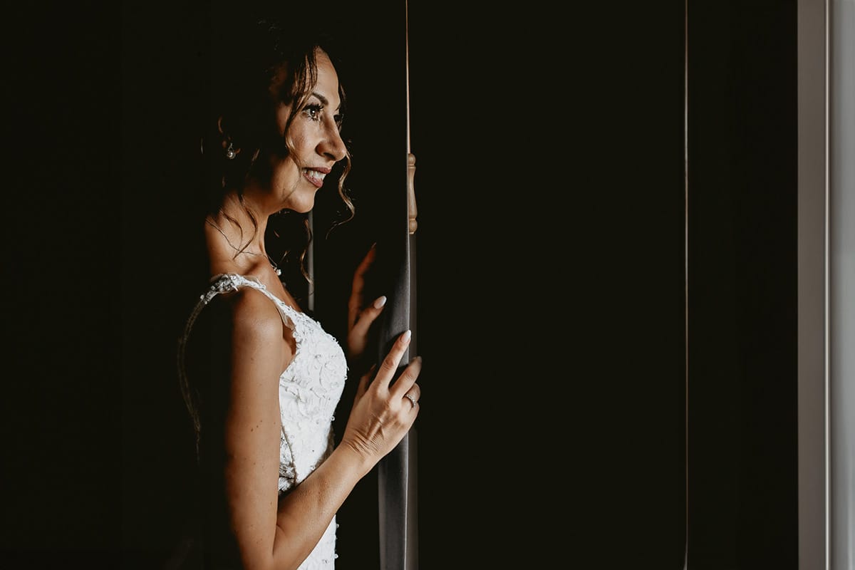 Matrimonio a "La Madernassa" nelle Langhe sotto la pioggia. Preparazione della sposa. Ritratto della sposa alla finestra.