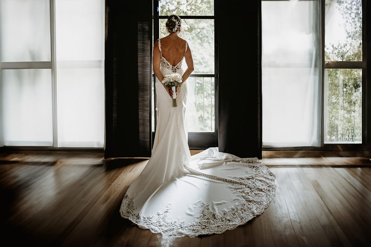 Matrimonio a "La Madernassa" nelle Langhe sotto la pioggia. Preparazione della sposa. Ritratto della sposa alla finestra. Figura intera.