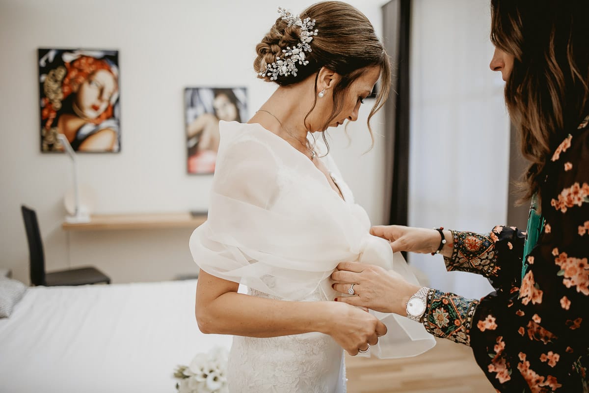 Wp mette una stola sulle spalle della sposa.Ritratto della sposa alla finestra.