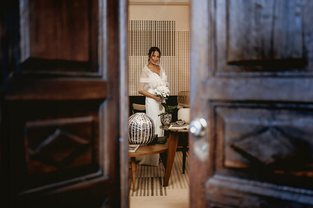 Matrimonio a "La Madernassa" nelle Langhe sotto la pioggia. Preparazione della sposa. Ritratto della sposa attraverso la porta di ingresso semiaperta.