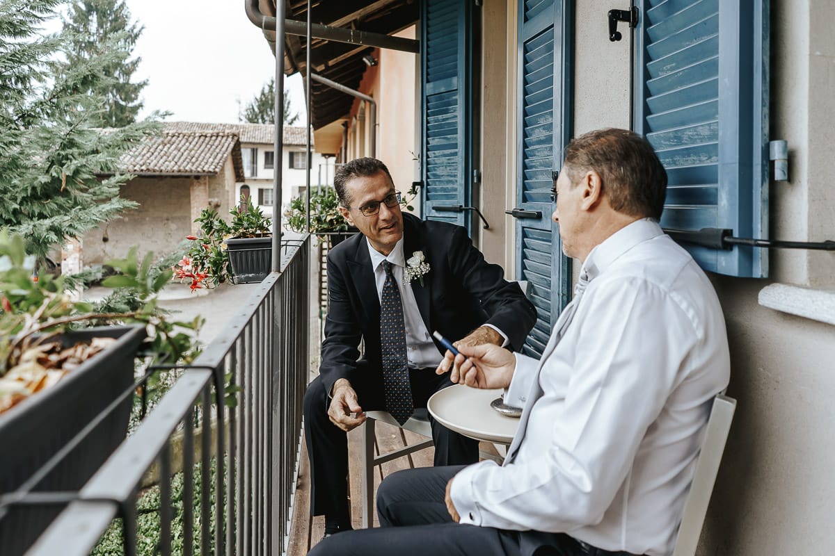 Matrimonio a "La Madernassa" nelle Langhe sotto la pioggia. preparazione dello sposo. Sposo conversa sul balcone con il testimone