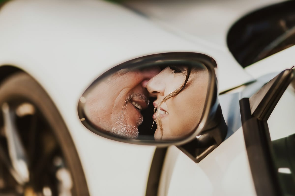 Post wedding a La Madernassa. Sposi all'esterno dentro la Porsche bianca. Sposi ripresi riflessi nello specchietto laterale.