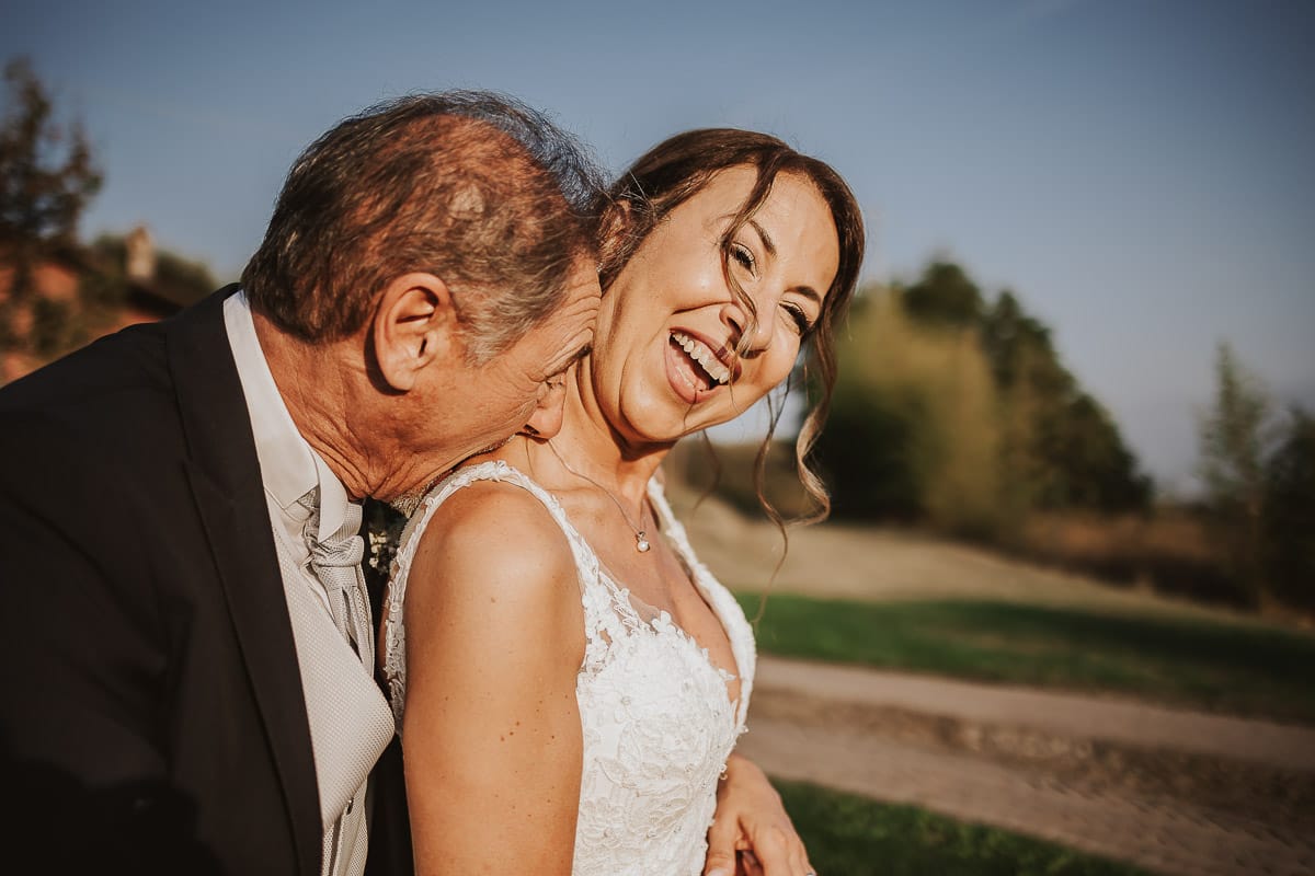 Post wedding a La Madernassa. Sposi seduti su di un muretto di mattoni sposo bacia la sposa sul collo.