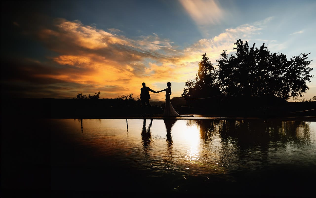 Post wedding a La Madernassa. Sposi passeggiano a bordo piscina al tramonto. Silhouette riflessa nella piscina.