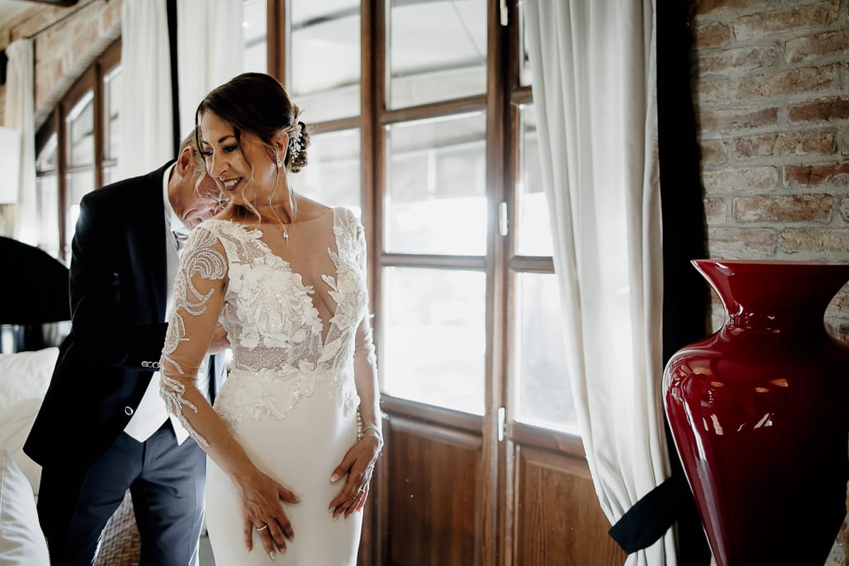 Post wedding a La Madernassa. Sposo abbottona l'abito della sposa.