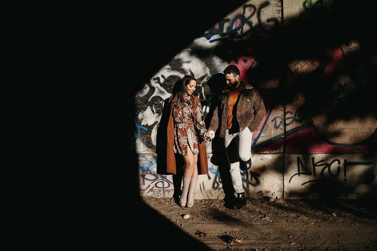 Prewedding a Torino, sul lungo Po al tramonto. Ritratto intimo della coppia sotto il ponte sul fiume. Chiaroscuro in una zona di graffiti metropolitani