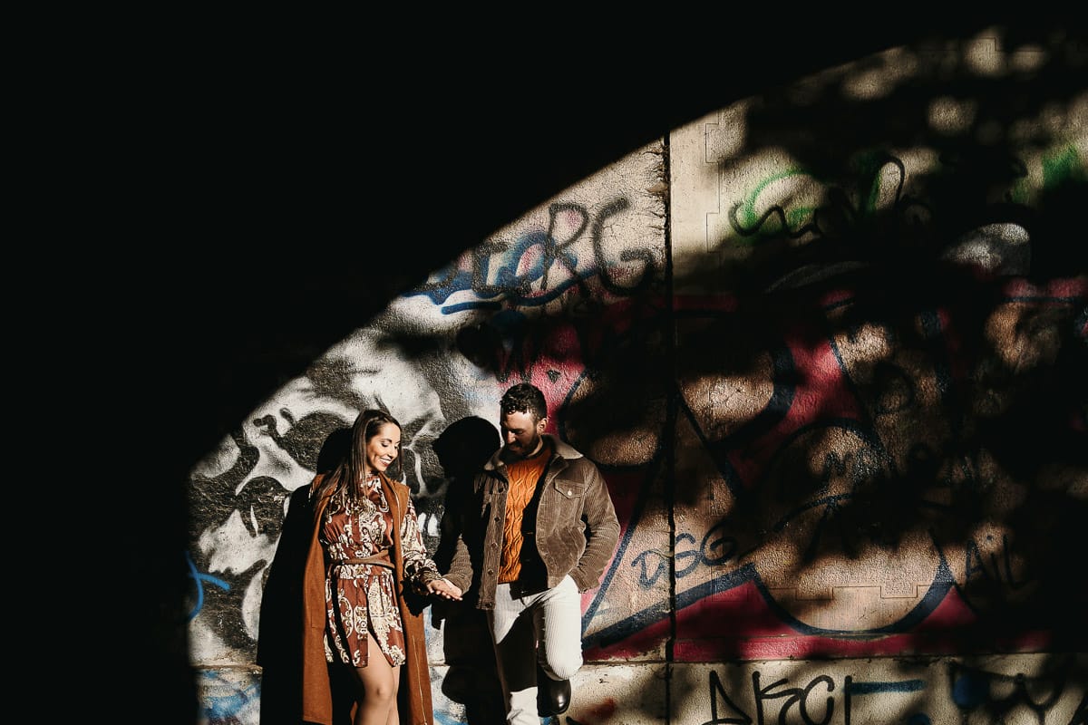 Prewedding a Torino, sul lungo Po al tramonto. Ritratto intimo della coppia sotto il ponte sul fiume. Chiaroscuro in una zona di graffiti metropolitani