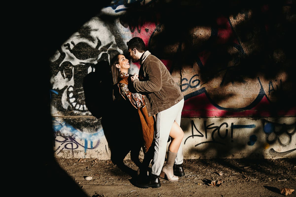 Prewedding a Torino, sul lungo Po al tramonto. Ritratto intimo della coppia sotto il ponte sul fiume. Chiaroscuro in una zona di graffiti metropolitani