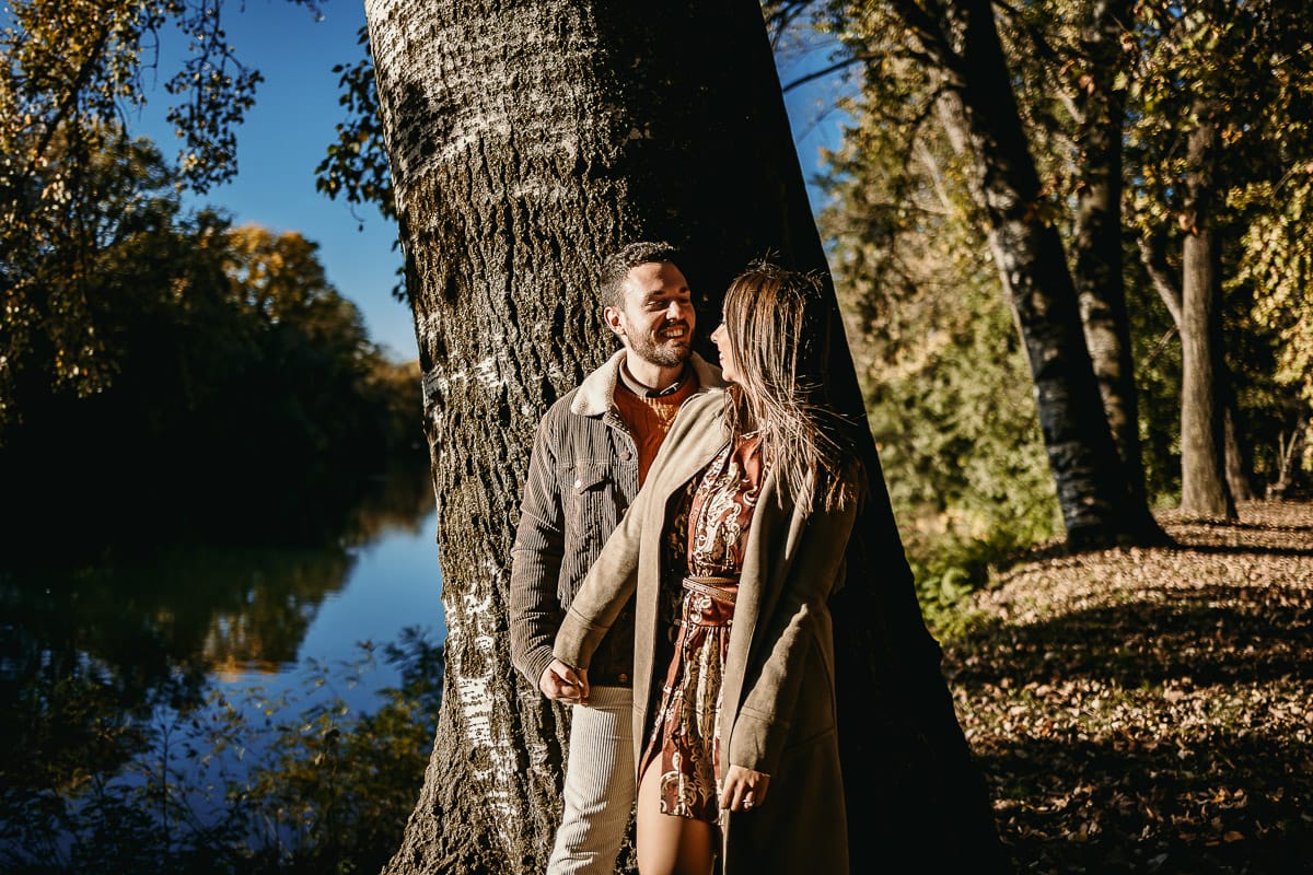 Prewedding a Torino, sul lungo Po al tramonto. La coppia si guarda appoggiata al tronco di un albero.