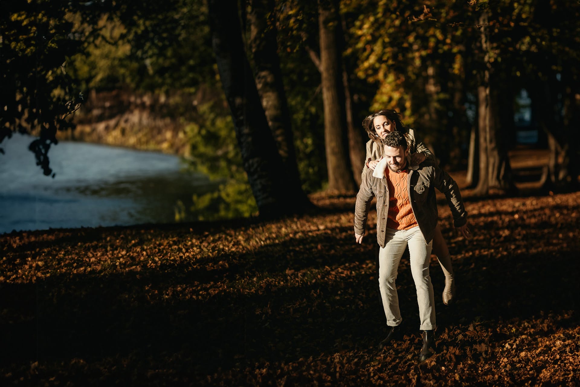 Prewedding a Torino, lungo il fiume Po in autunno. Coppia gioca. Ragazza salta in groppa al ragazzo.