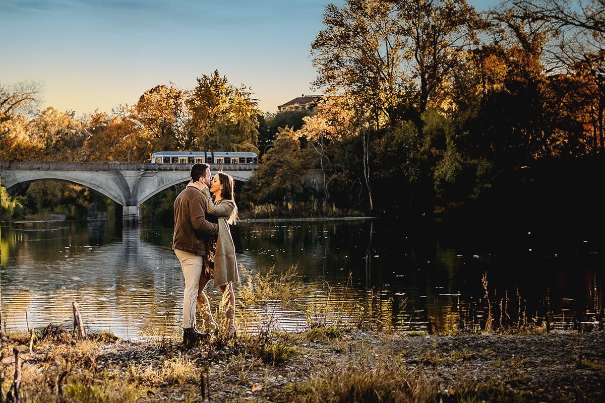 Prewedding a Torino, sul lungo Po al tramonto. Ritratto sulla riva del fiume con la magia dell'autunno sull'acqua. Sullo sfondo il ponte sul quale sta passando un tram.