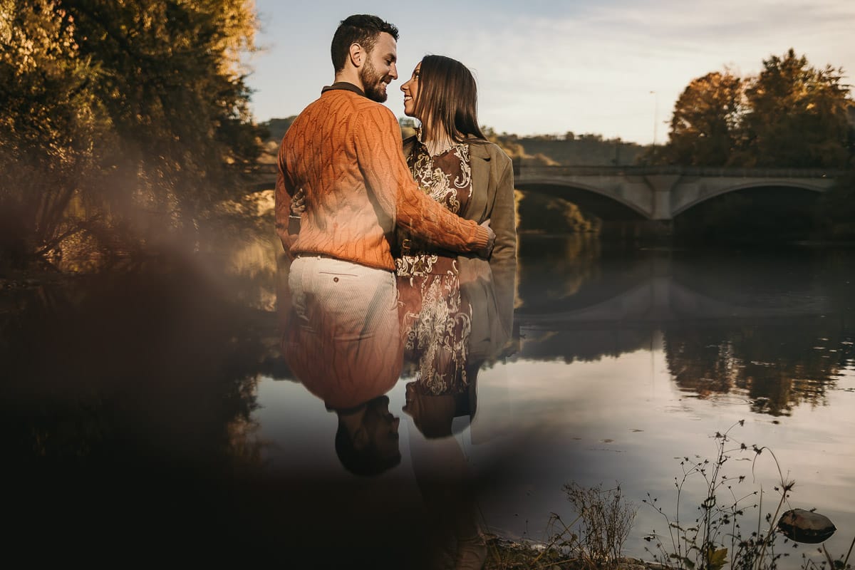 Prewedding a Torino, sul lungo Po al tramonto. Ritratto sulla riva del fiume con la magia dell'autunno sull'acqua. Sullo sfondo il ponte. Riflessi in uno specchio.