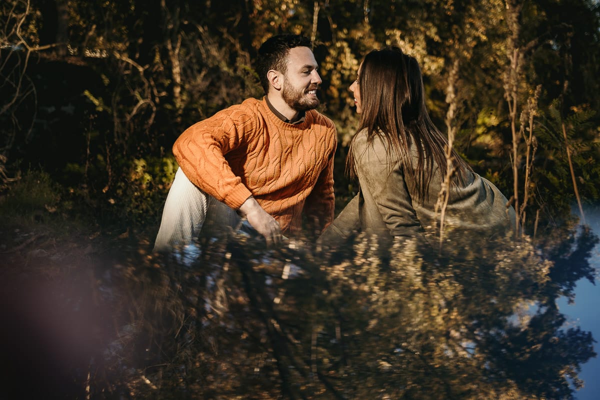 Prewedding a Torino, sul lungo Po al tramonto. Ritratto sulla riva del fiume con la magia dell'autunno sull'acqua. Coppia seduta si guarda