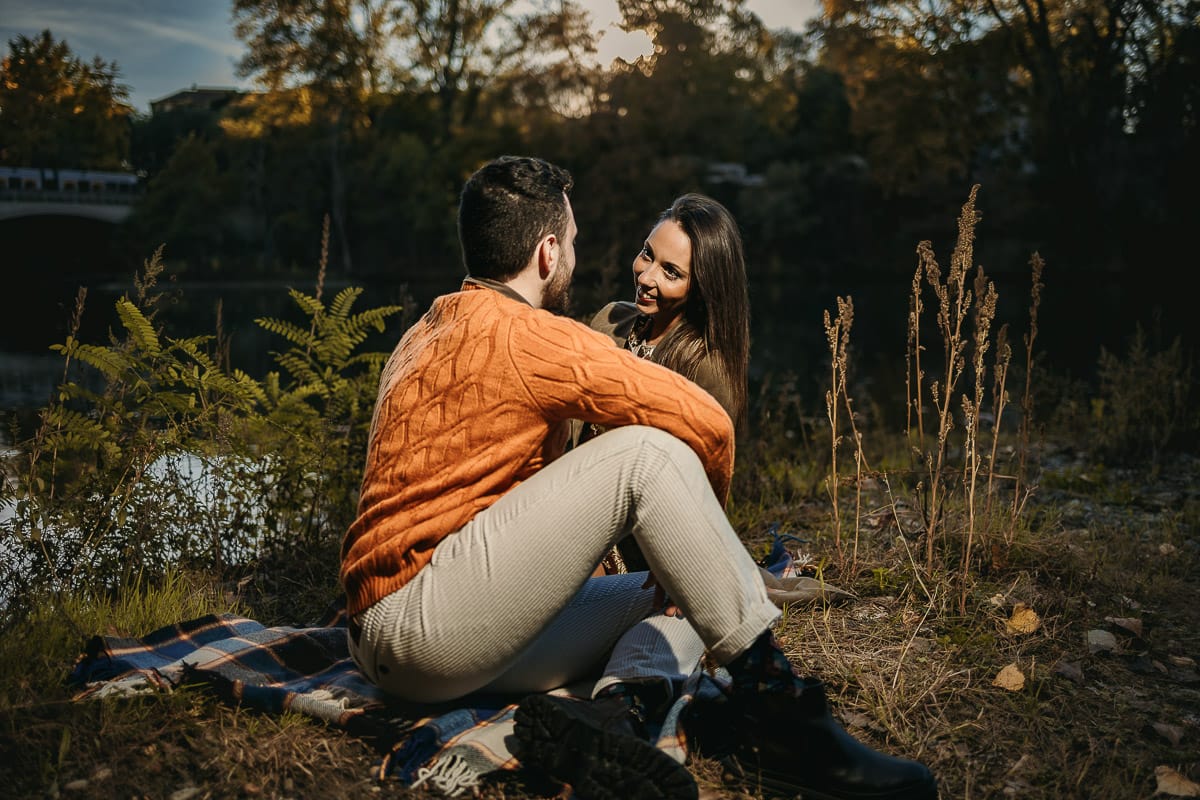Prewedding a Torino, sul lungo Po al tramonto. Ritratto sulla riva del fiume con la magia dell'autunno sull'acqua. Coppia seduta