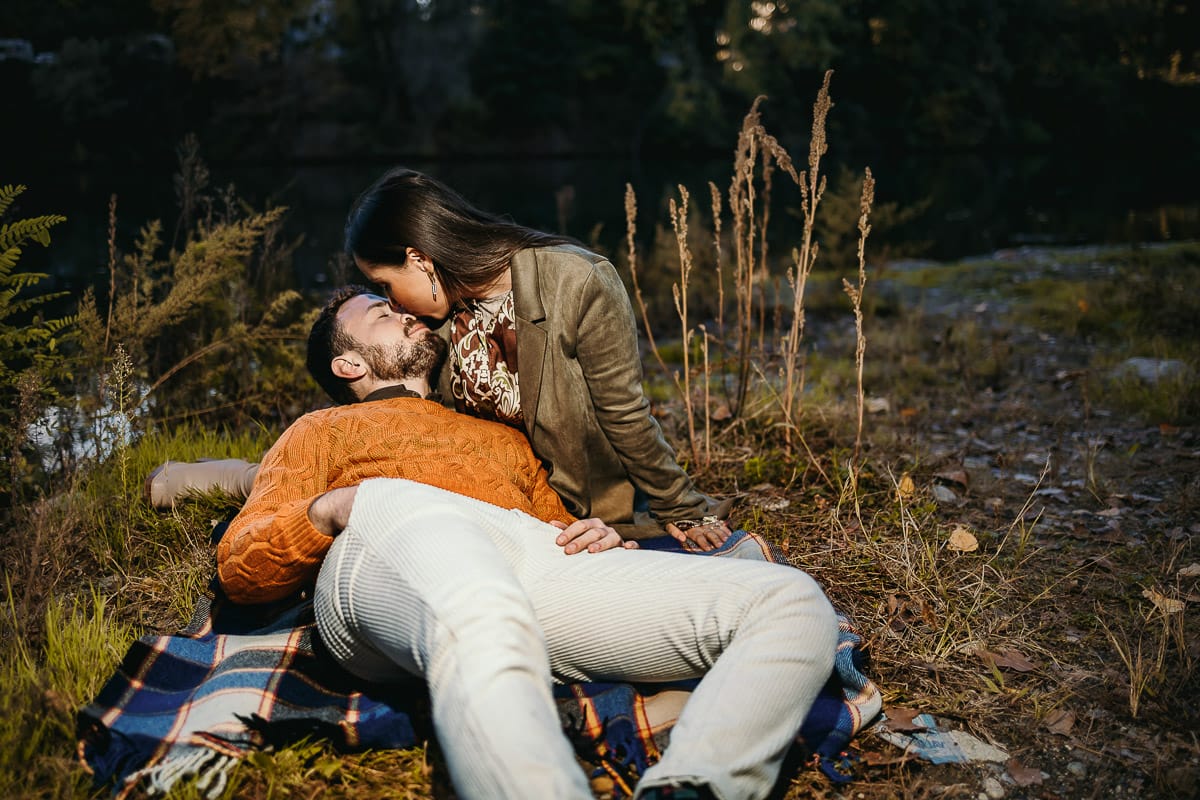Prewedding a Torino, sul lungo Po al tramonto. Ritratto sulla riva del fiume con la magia dell'autunno sull'acqua. Coppia seduta