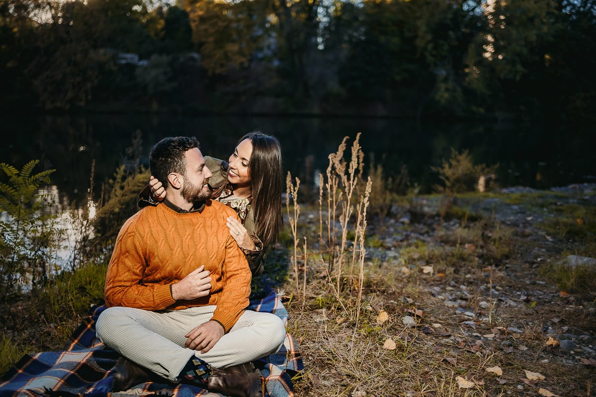 Prewedding a Torino, sul lungo Po al tramonto. Ritratto sulla riva del fiume con la magia dell'autunno sull'acqua. Coppia seduta