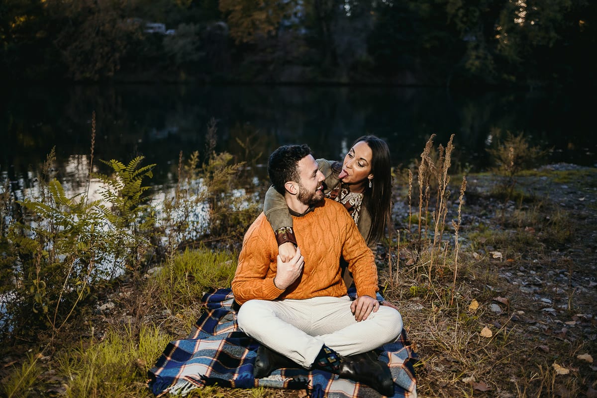 Prewedding a Torino, sul lungo Po al tramonto. Ritratto sulla riva del fiume con la magia dell'autunno sull'acqua. Coppia seduta