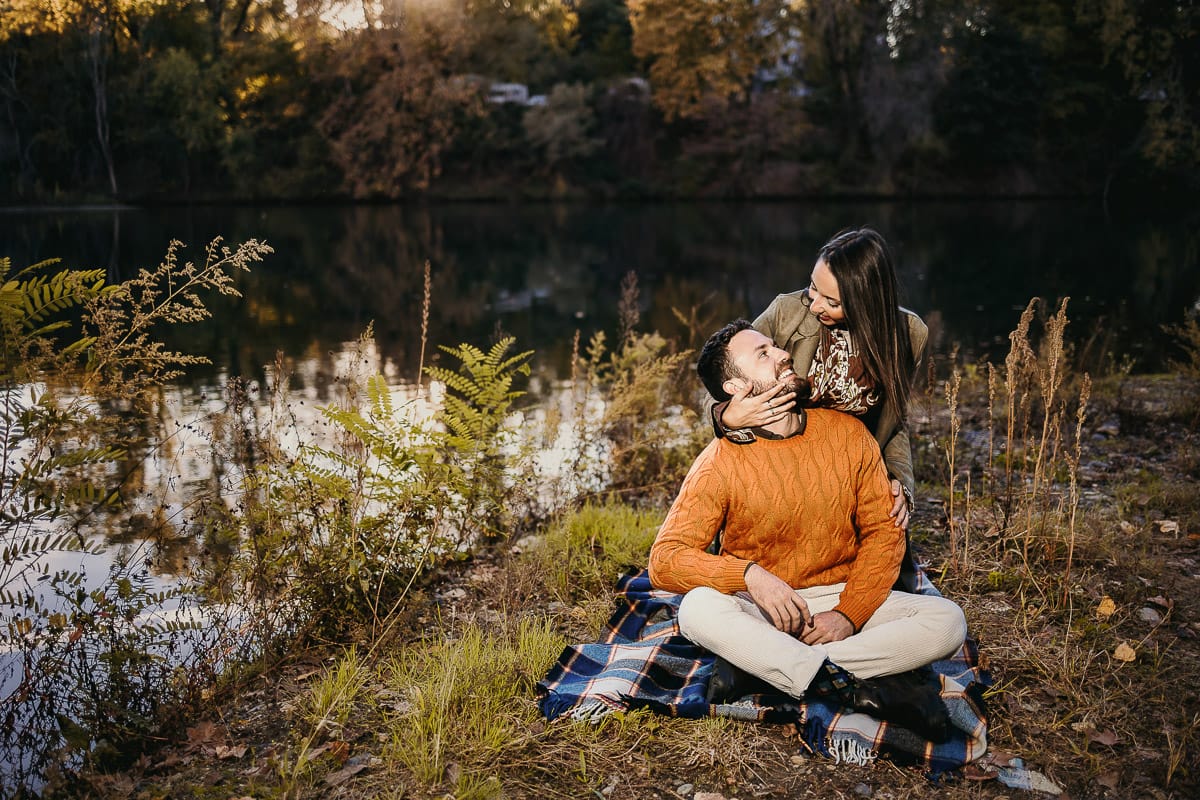 Prewedding a Torino, sul lungo Po al tramonto. Ritratto sulla riva del fiume con la magia dell'autunno sull'acqua. Coppia seduta
