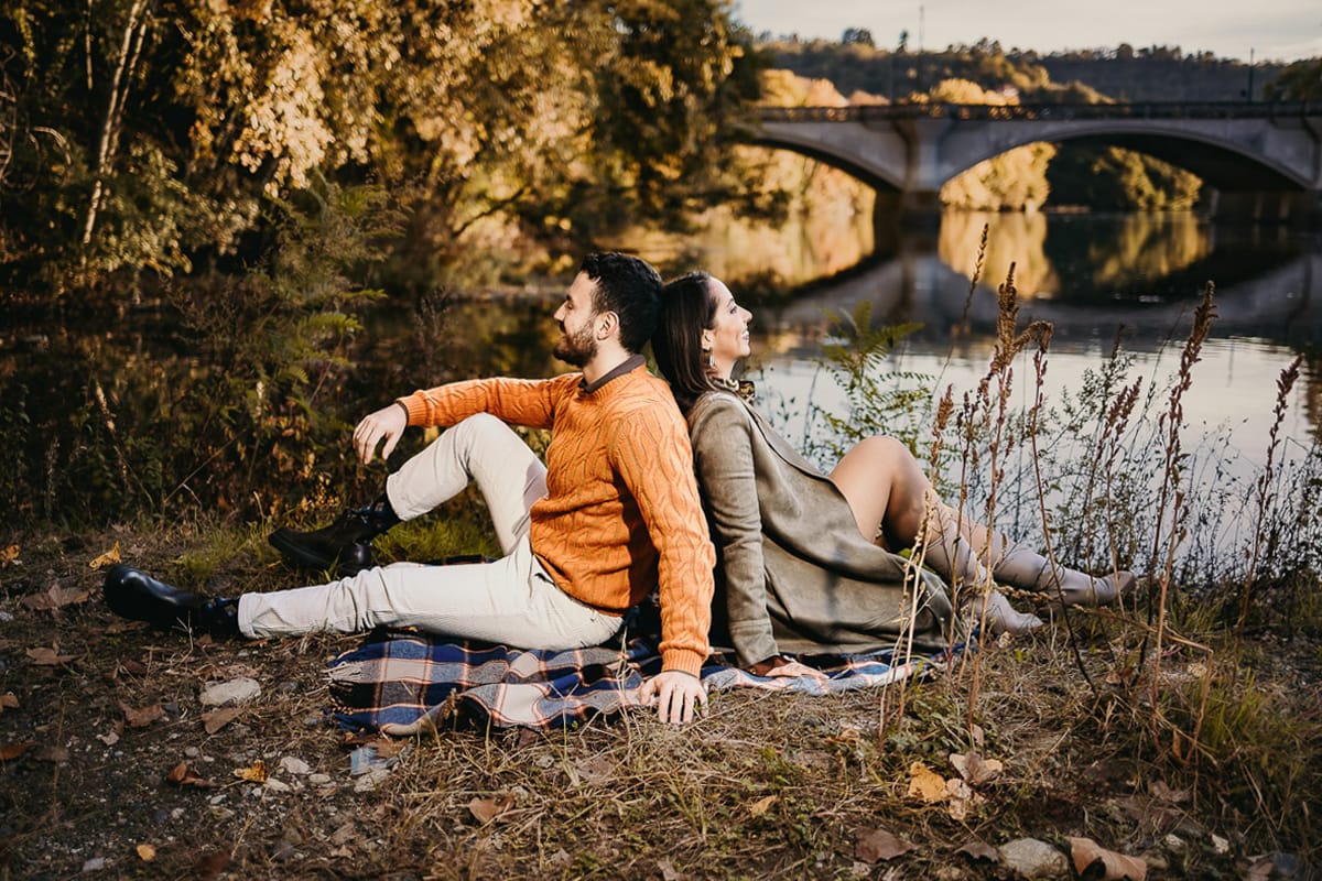 Prewedding a Torino, sul lungo Po al tramonto. Ritratto sulla riva del fiume con la magia dell'autunno sull'acqua. Coppia seduta