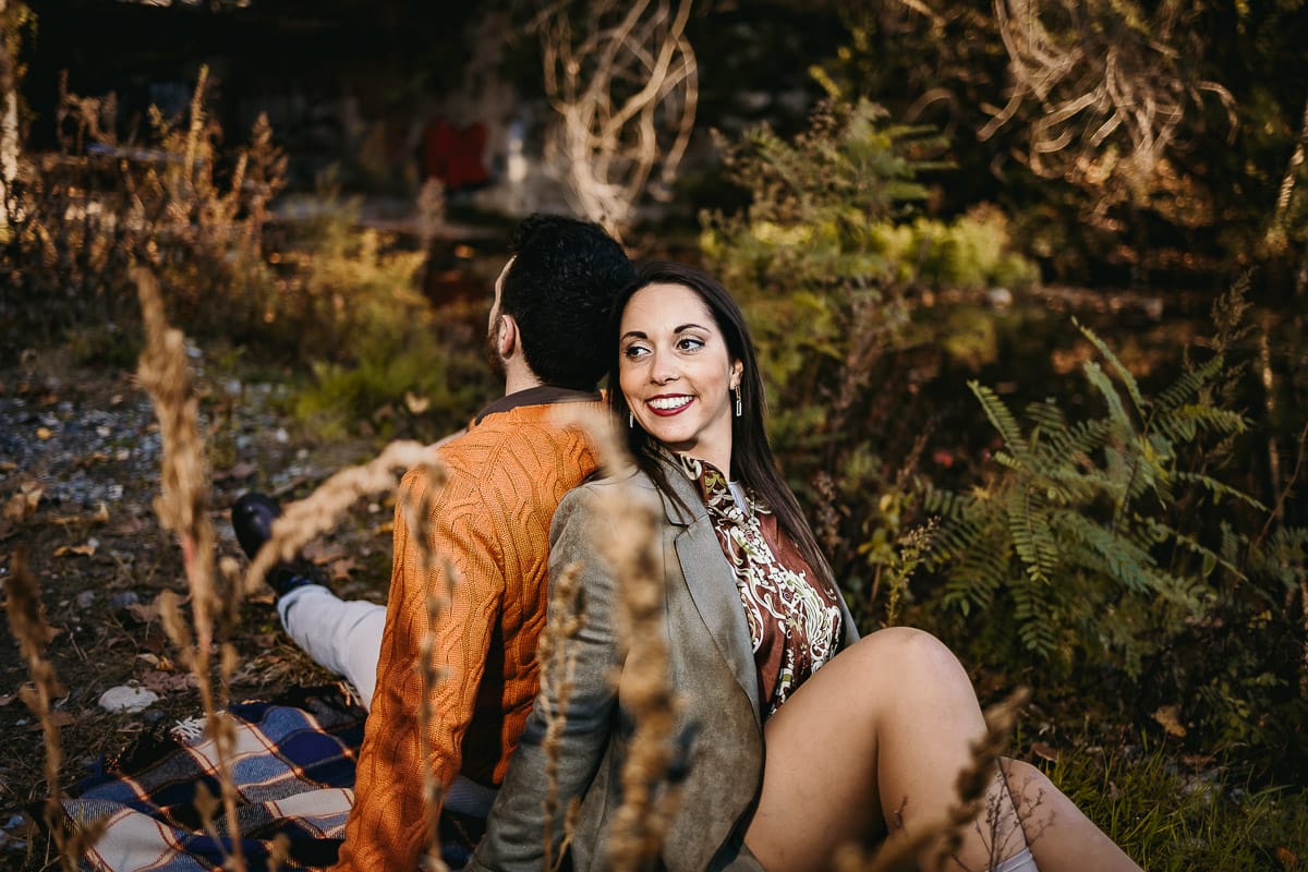 Prewedding a Torino, sul lungo Po al tramonto. Ritratto sulla riva del fiume con la magia dell'autunno sull'acqua. Coppia seduta