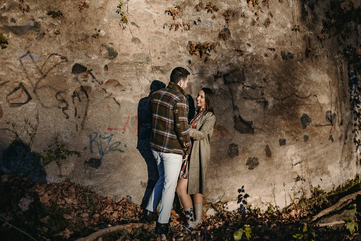 Prewedding a Torino, sul lungo Po al tramonto. Ritratto sulla riva del fiume con la magia dell'autunno sull'acqua. Coppia contro un pilastro di sostegno ddi un ponte.