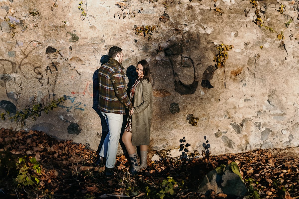 Prewedding a Torino, sul lungo Po al tramonto. Ritratto sulla riva del fiume con la magia dell'autunno sull'acqua. Coppia contro un pilastro di sostegno ddi un ponte.