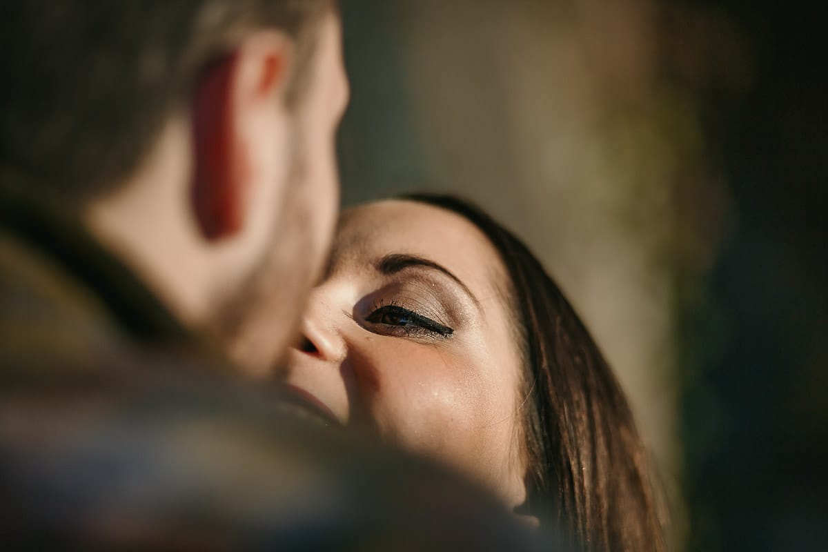 Prewedding a Torino, sul lungo Po al tramonto. Ritratto sulla riva del fiume con la magia dell'autunno sull'acqua. Coppia contro un pilastro di sostegno ddi un ponte.