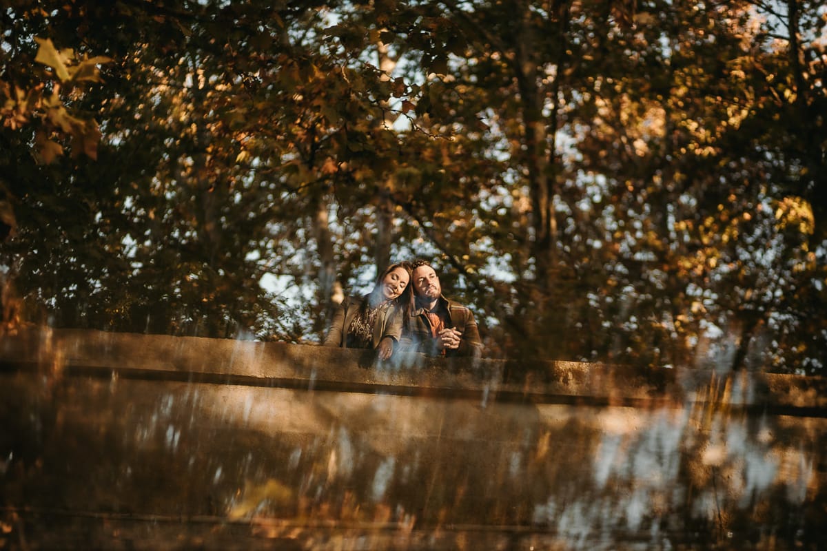 Prewedding a Torino, sul lungo Po al tramonto. Ritratto sulla riva del fiume con la magia dell'autunno sull'acqua. Coppia sul ponticello in mezzo agli alberi. Riflessi.