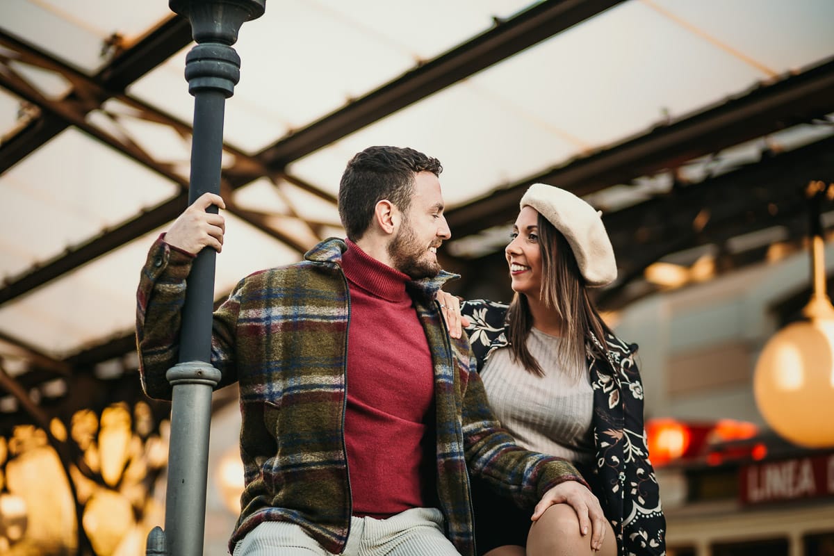 Prewedding a Torino, nella stazione di Sassi. Coppia seduta sul cancelletto di ferro davanti ai trenini a cremagliera che portano a Superga