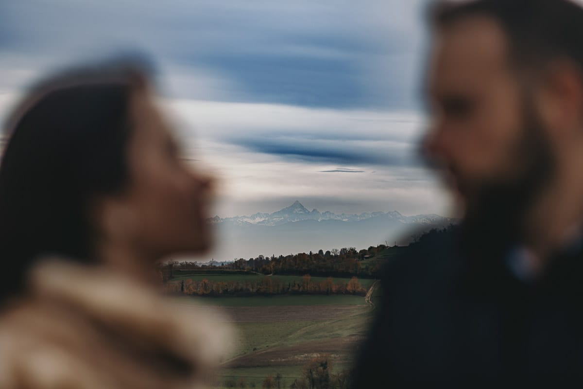 Fotografia di coppia invernale presso la chiesa di San Lorenzo di Mombello di Torino. Barbara e Riccardo fuori fuoco. in mezzo a loro in lontananza il profilo del Monviso.