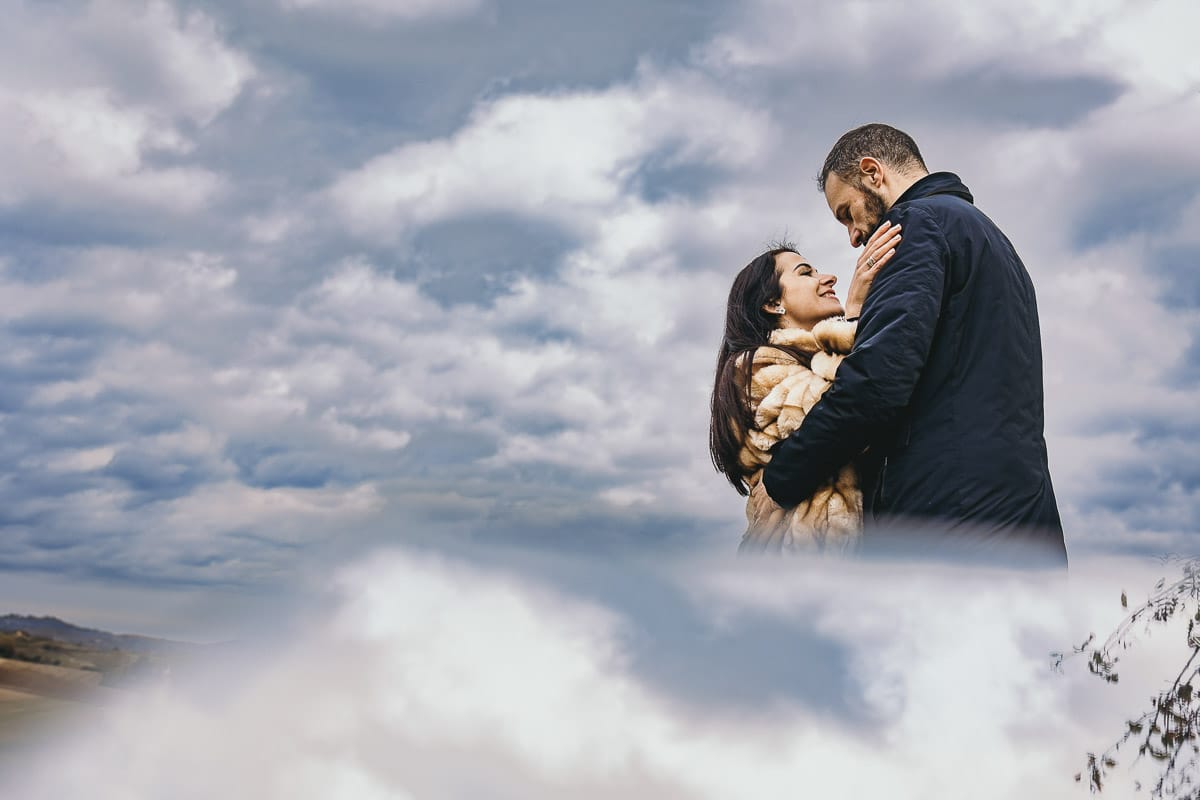 Fotografia di coppia invernale presso la chiesa di San Lorenzo di Mombello di Torino. Barbara e Riccardo tra le nuvole.Ritratto riflesso con un piccolo specchio
