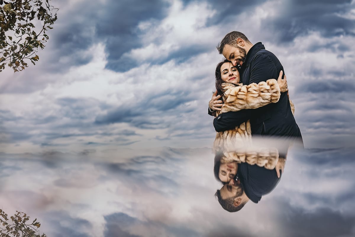 Fotografia di coppia invernale presso la chiesa di San Lorenzo di Mombello di Torino. Barbara e Riccardo tra le nuvole.Ritratto riflesso con un piccolo specchio