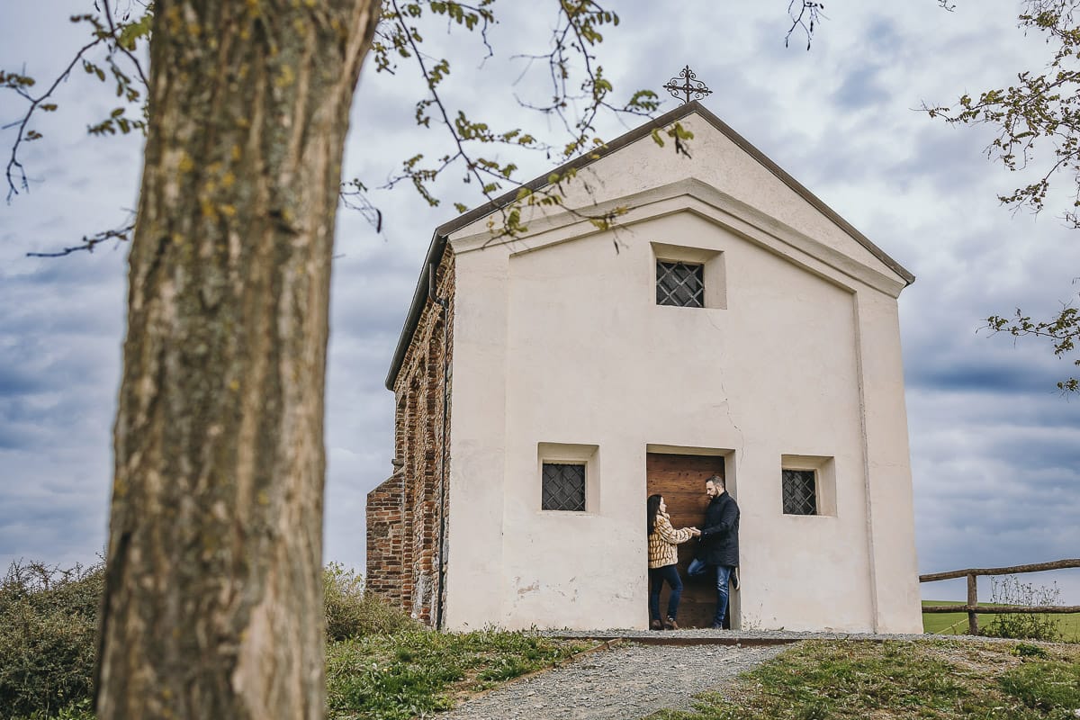 Fotografia di coppia invernale presso la chiesa di San Lorenzo di Mombello di Torino. Barbara e Riccardo davanti alla porta di legno della chiesetta