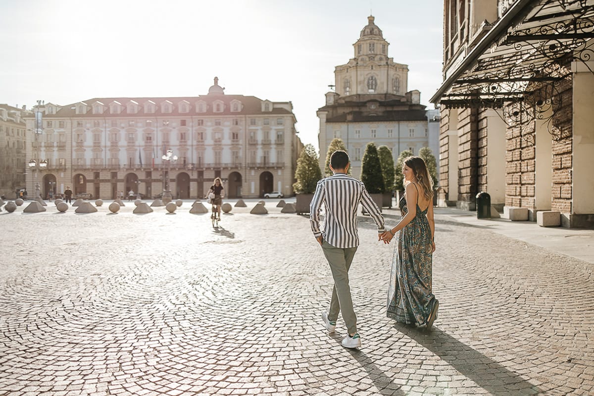 Prewedding nel centro di Torino Elisa e Davide camminano in piazza Castello. Sullo sfondo la cappella della Sindone e il palazzo della Regione