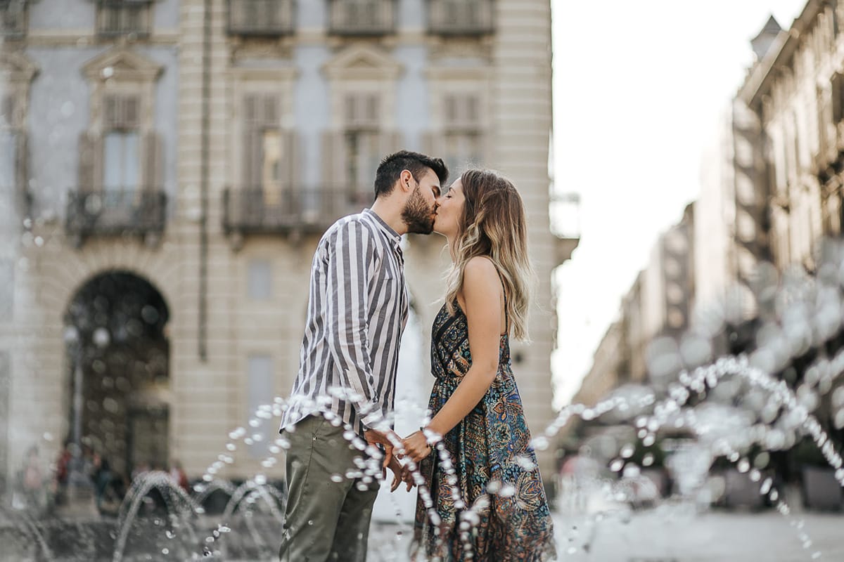Prewedding nel centro di Torino Elisa e Davide in piazza Castello dietro alle fontane si baciano