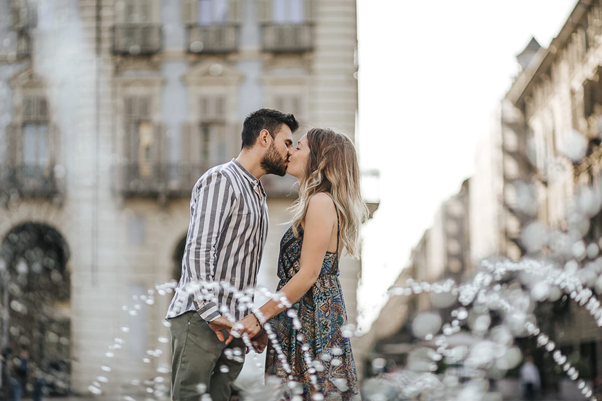 Prewedding nel centro di Torino Elisa e Davide in piazza Castello dietro alle fontane si baciano