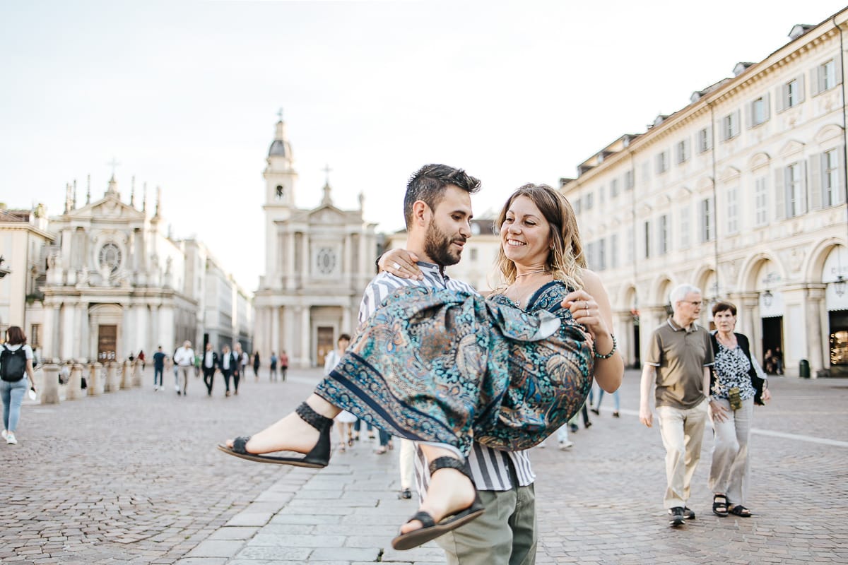 Prewedding nel centro di Torino Elisa e Davide in piazza San Carlo. Davide prende in braccio Elisa.