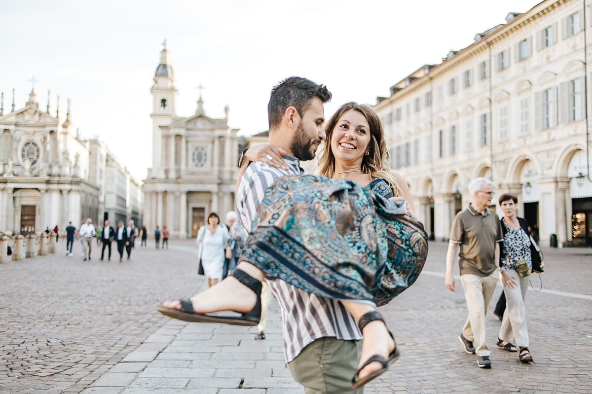 Prewedding nel centro di Torino Elisa e Davide in piazza San Carlo. Davide prende in braccio Elisa.