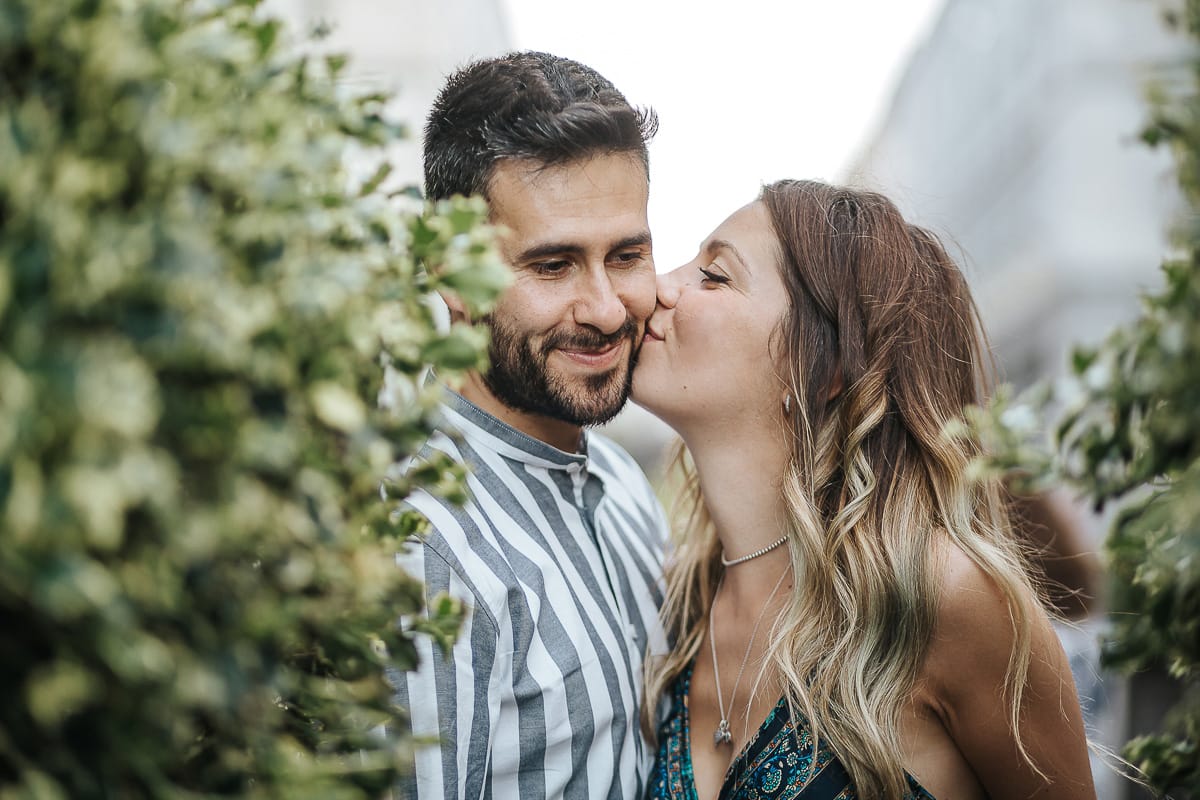 Prewedding nel centro di Torino Elisa e Davide in piazza CLN ritratto ravvicinato tra i vasi topiari Elisa bacia Davide sulla guancia