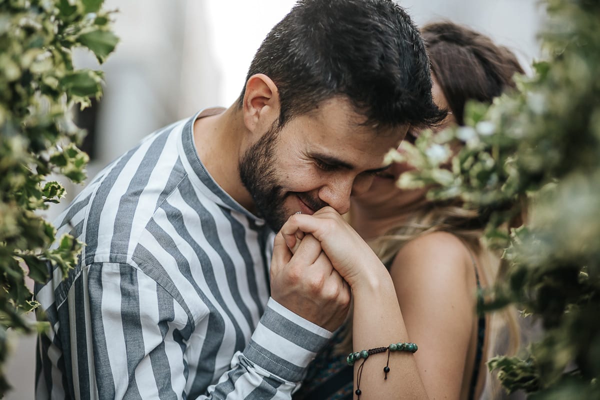 Prewedding nel centro di Torino Elisa e Davide in piazza CLN ritratto ravvicinato tra i vasi topiari. Davide bacia la mano di Elisa sull'anello di fidanzamento