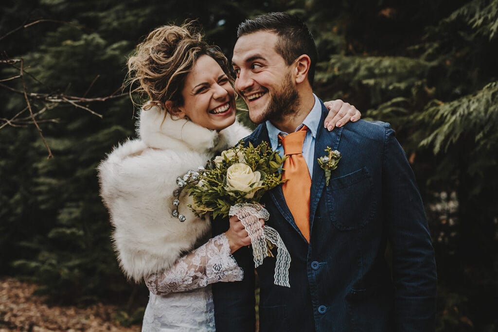 Winter wedding at the Superga hill park, among coniferous trees reminiscent of the great parks of North America. The bride and groom laugh happily.