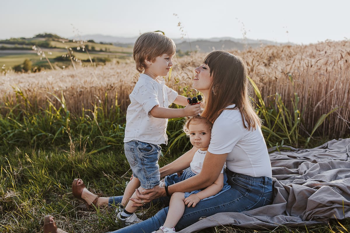 Foto di Famiglia al Tramonto: Ilenia, Filippo, Edoardo e Camilla a Mombello di Torino. la famiglia seduta in un sentiero tra due campi di grano. Il bambino sta per baciare la mma.