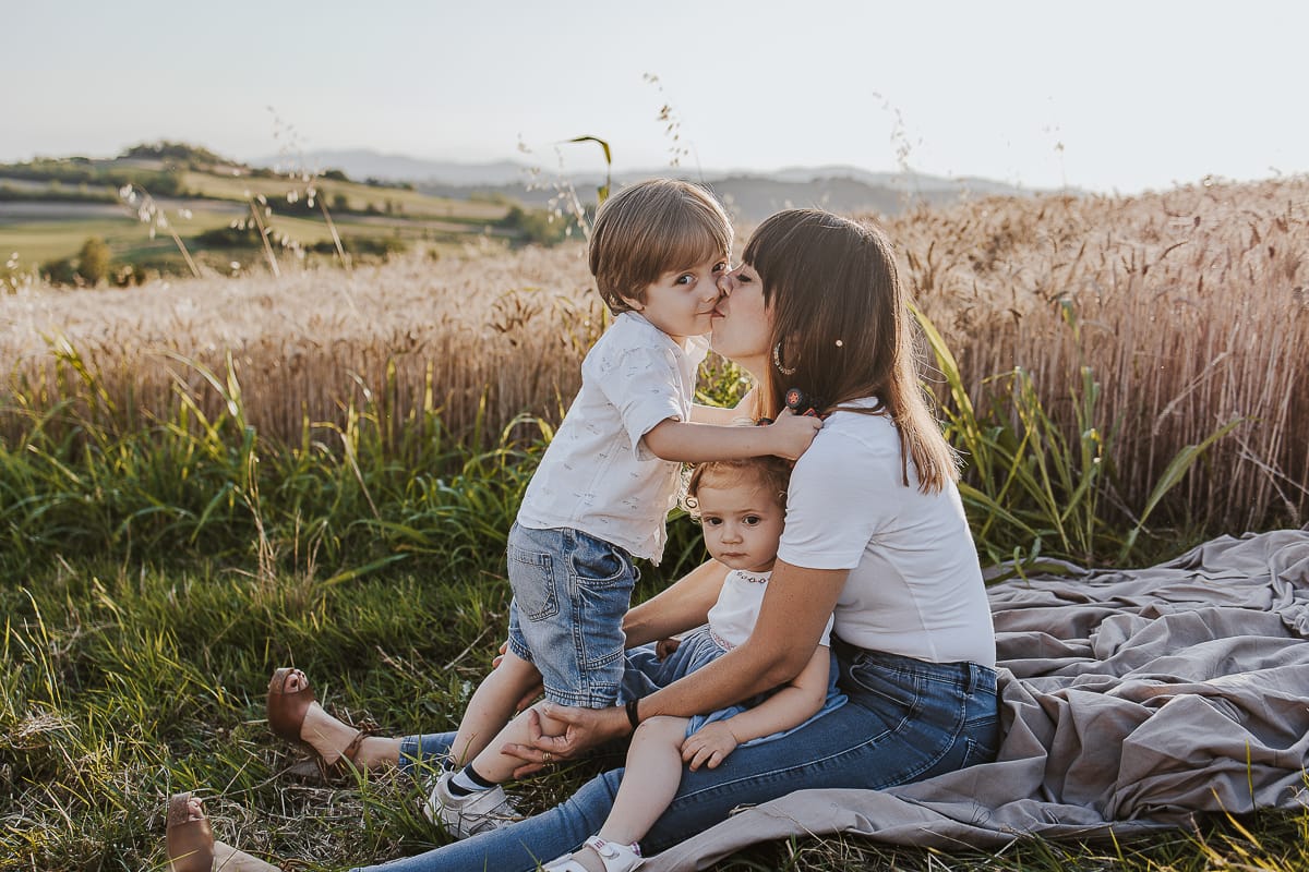 Foto di Famiglia al Tramonto: Ilenia, Filippo, Edoardo e Camilla a Mombello di Torino. la famiglia seduta in un sentiero tra due campi di grano.Il tenero gesto di un bambino che dimostra il suo amore per la mamma