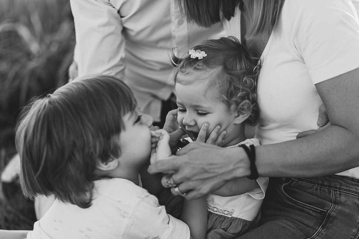 Foto di Famiglia al Tramonto: Ilenia, Filippo, Edoardo e Camilla a Mombello di Torino. la famiglia seduta in un sentiero tra due campi di grano.Il tenero gesto di un bambino che dimostra il suo amore per la sorellina