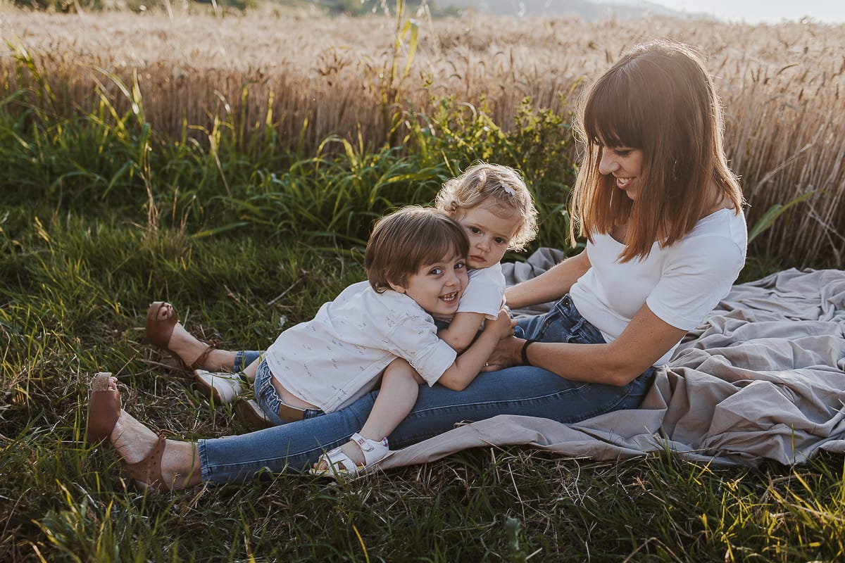 Foto di Famiglia al Tramonto: Ilenia, Filippo, Edoardo e Camilla a Mombello di Torino. la famiglia seduta in un sentiero tra due campi di grano.Il tenero gesto di un bambino che dimostra il suo amore per la sorellina