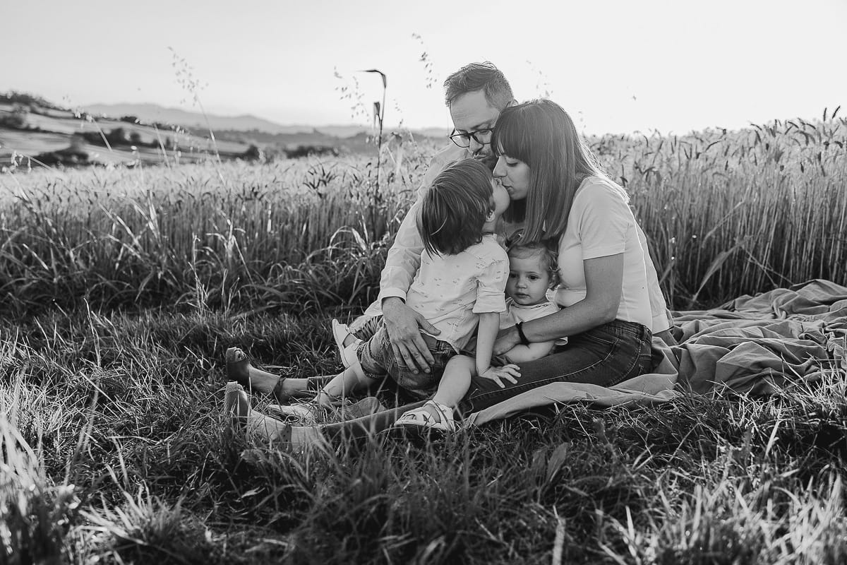 Foto di Famiglia al Tramonto: Ilenia, Filippo, Edoardo e Camilla a Mombello di Torino. la famiglia seduta in un sentiero tra due campi di grano.Il tenero gesto di un bambino che dimostra il suo amore per la mamma